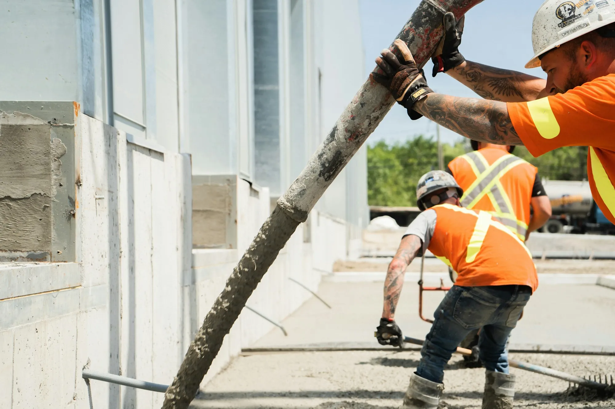 Crew placing concrete from a pump hose beside a wall
